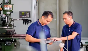 Engenheiros a inspecionar uma peça metálica no chão de fábrica durante uma auditoria à qualidade do fornecedor.