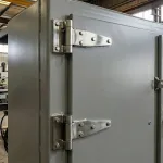 Charnières externes à sangle boulonnées à l'extérieur d'une porte d'armoire industrielle dans un atelier.