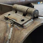 Weld-on hinge fillet-welded to a round steel post, showing mounting without a flat surface